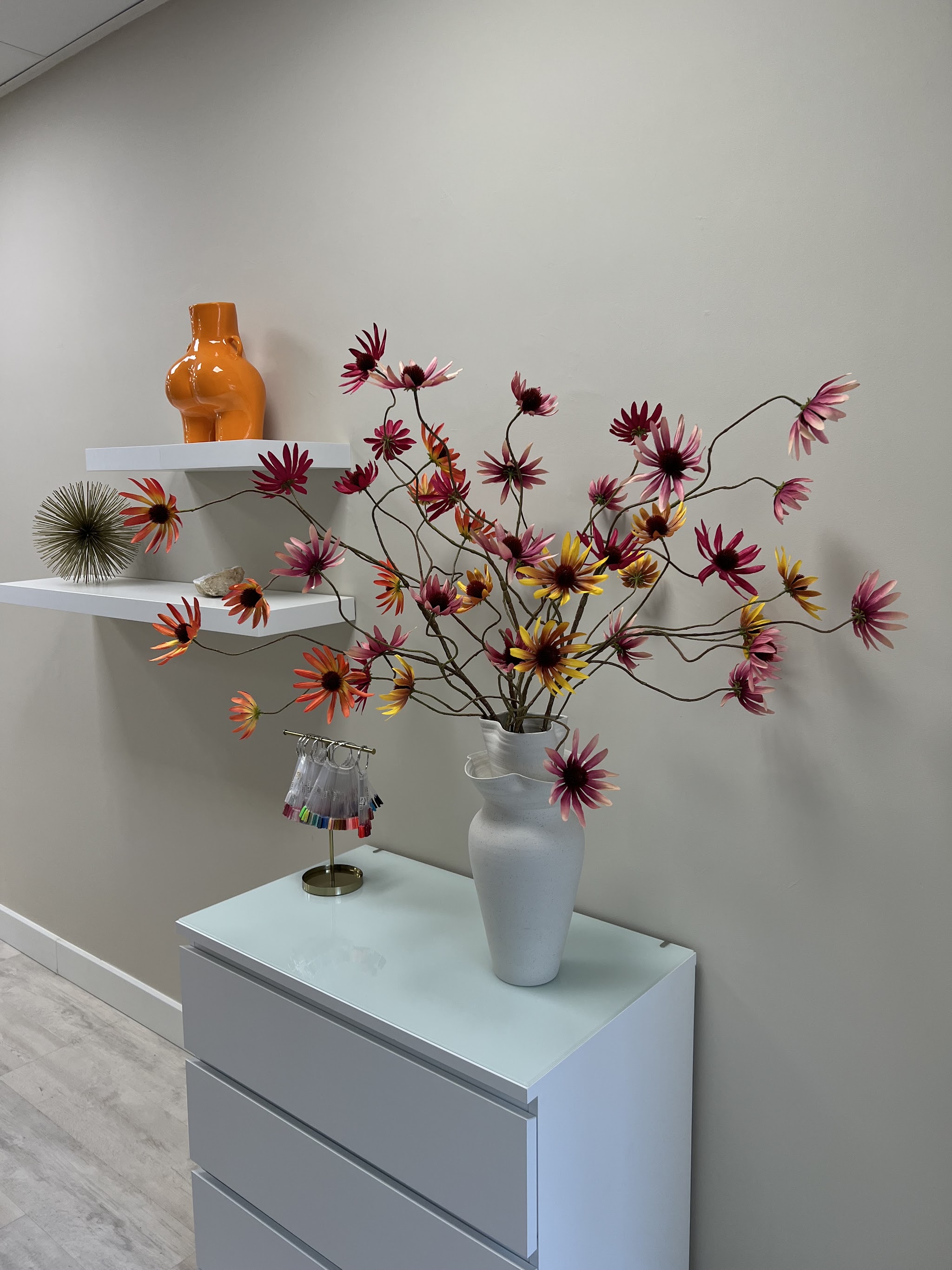 Oranje vaas met bloemstuk op een witte kast